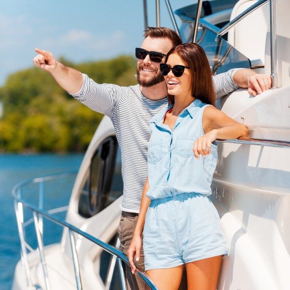 This view is amazing! Cheerful young couple looking away and smiling while standing on the board of yacht